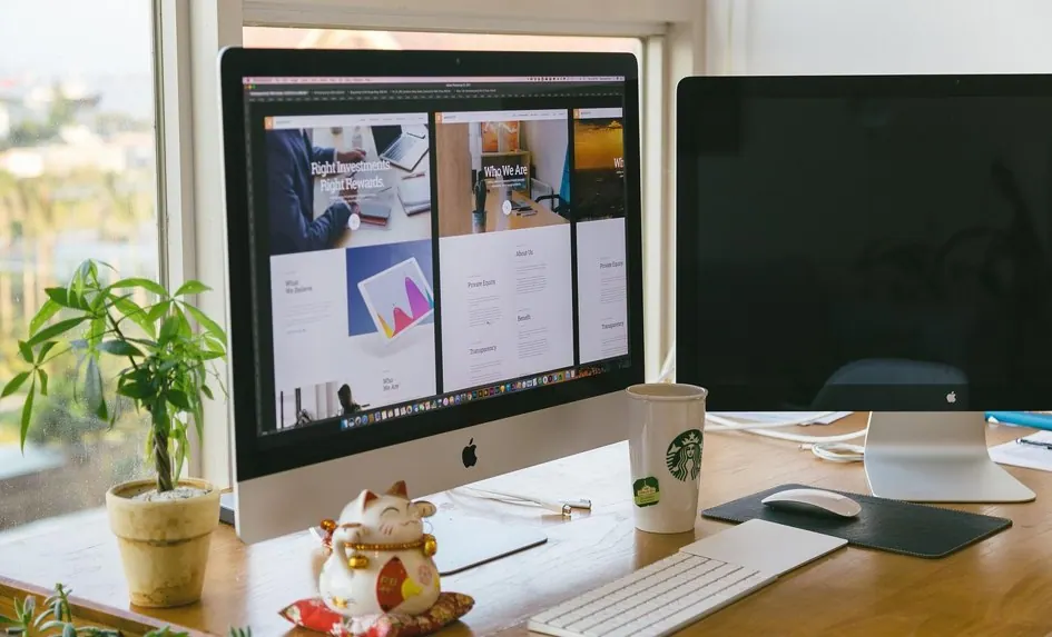 Zwei große Monitore zeigen einen modernen Website-Entwurf an einem hellen Arbeitsplatz.